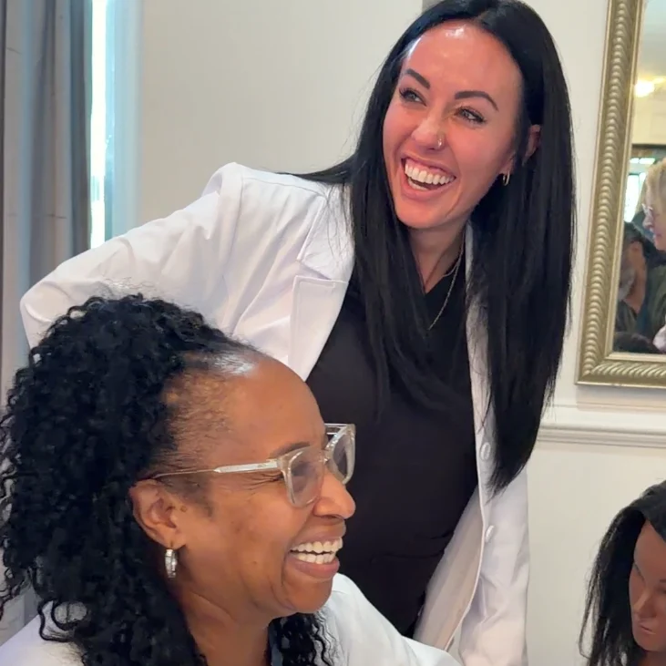 Two smiling USTI trichologists in lab coats during a hands-on class